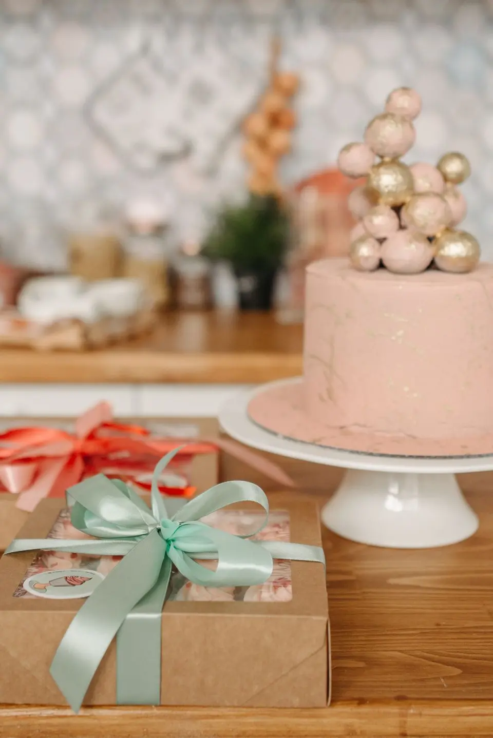 Torta rosada con esferas doradas junto a cajas de regalo